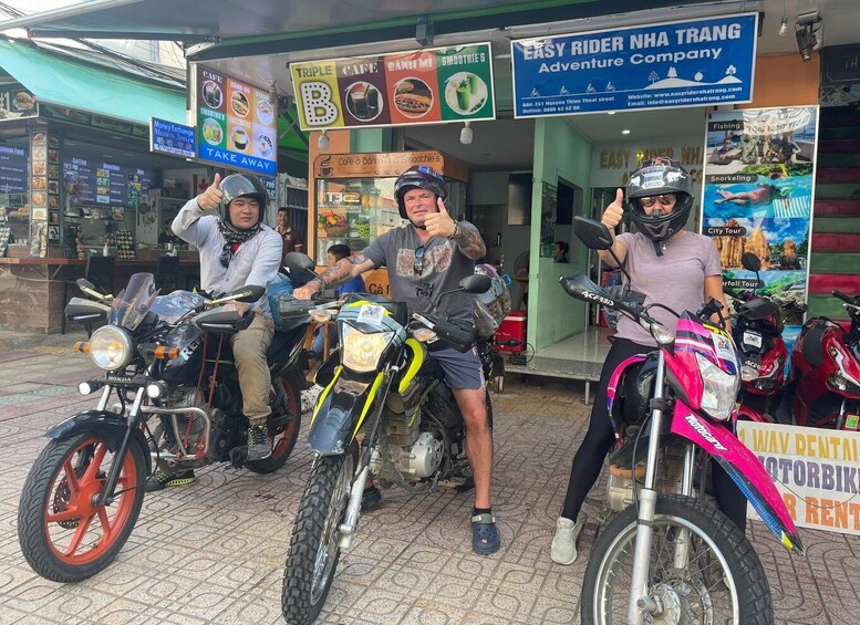 Three motorcyclists posing in front of a cafe and adventure company. 3