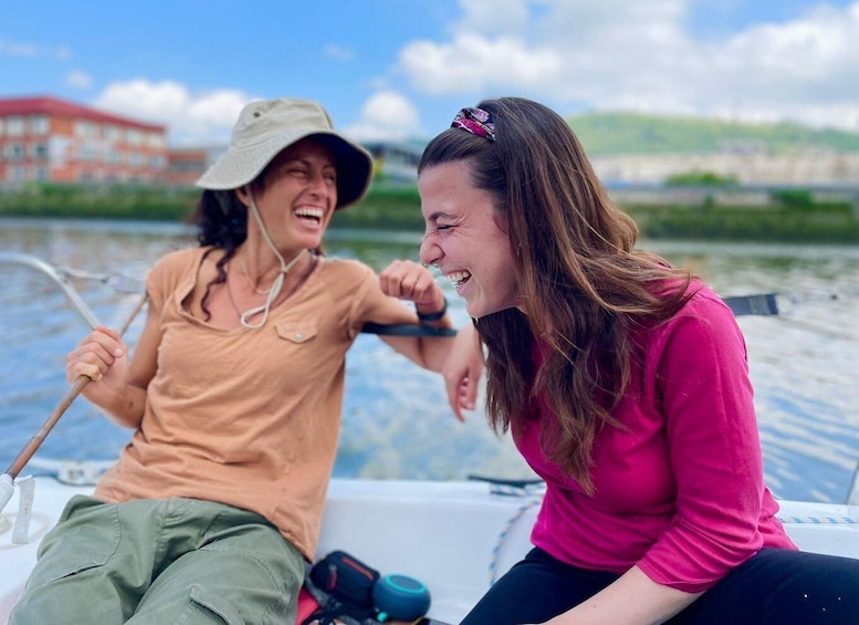 Two people on a boat, one holding a paddle, with a building and greenery in the background. 4