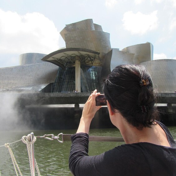 A person taking a photo of a modern architectural building with a unique design, near a body of water. 1