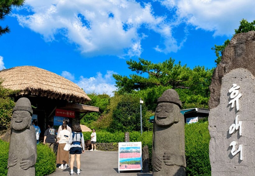 A stone entrance with a thatched-roof structure, a signboard, and a large stone figure. 3
