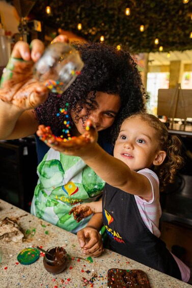 A person pouring colorful sprinkles onto a chocolate-covered treat. 3