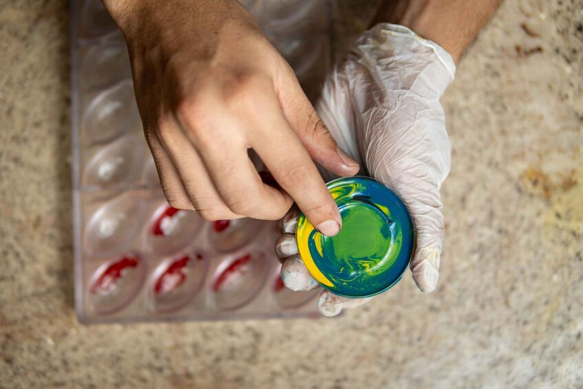 A person wearing gloves holding a small container with a green and yellow liquid. 5