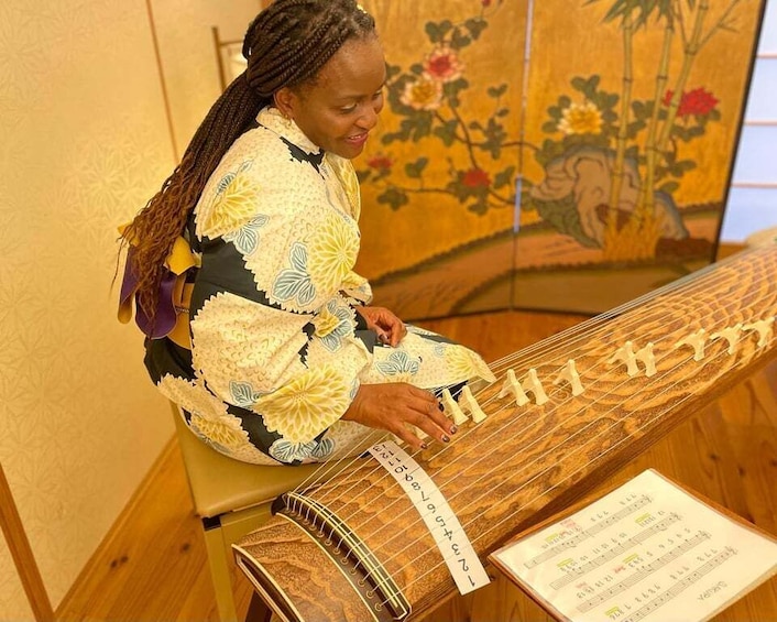 En person som spelar ett traditionellt stränginstrument med ett dekorativt skydd och ett notblad framför sig. 1