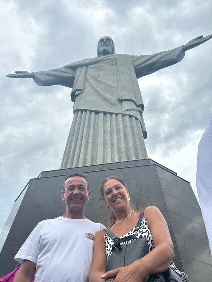 A couple standing in front of a large statue with outstretched arms. 2