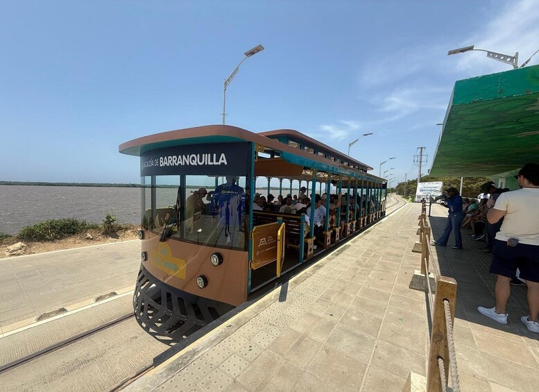 A cable car with passengers, a body of water, and a green structure in the background. 3