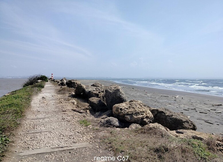 A coastal path with large rocks, a distant lighthouse, and a city skyline in the background. 5