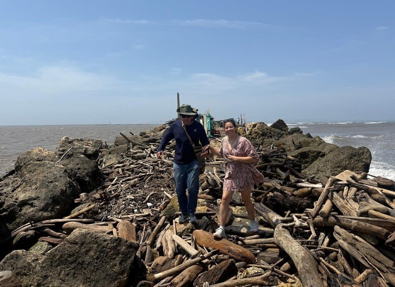 A rocky shoreline with driftwood and a person in a hat. 4