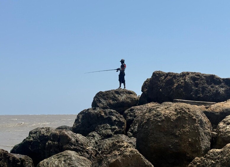 A person fishing on a rocky outcrop by the sea. 5