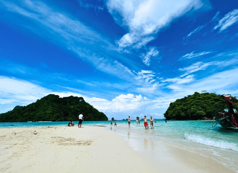 A beach with people walking and playing in the water, surrounded by lush green hills. 2