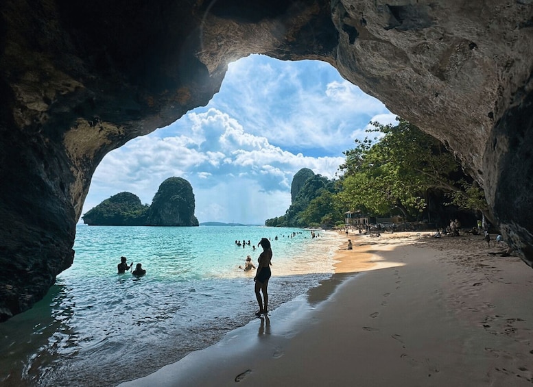 A beach with a cave entrance, turquoise water, and distant islands. 1