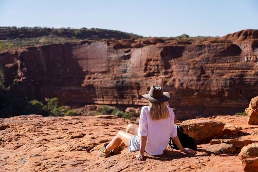 A person sitting on a red rock with a desert landscape in the background. 1
