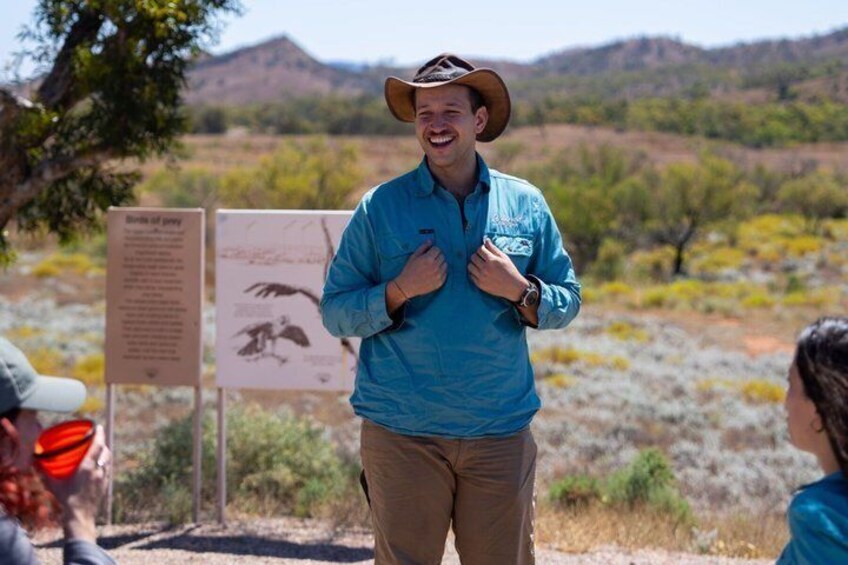 A person in a blue shirt and cowboy hat standing in a desert landscape with signs in the background. 3
