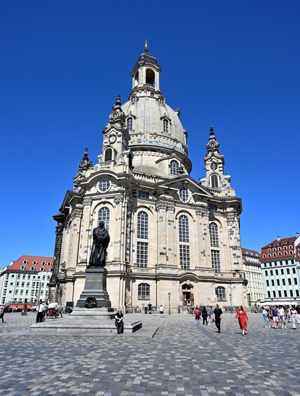 A historic building with a large dome and statues, surrounded by a cobblestone square with people walking. 5