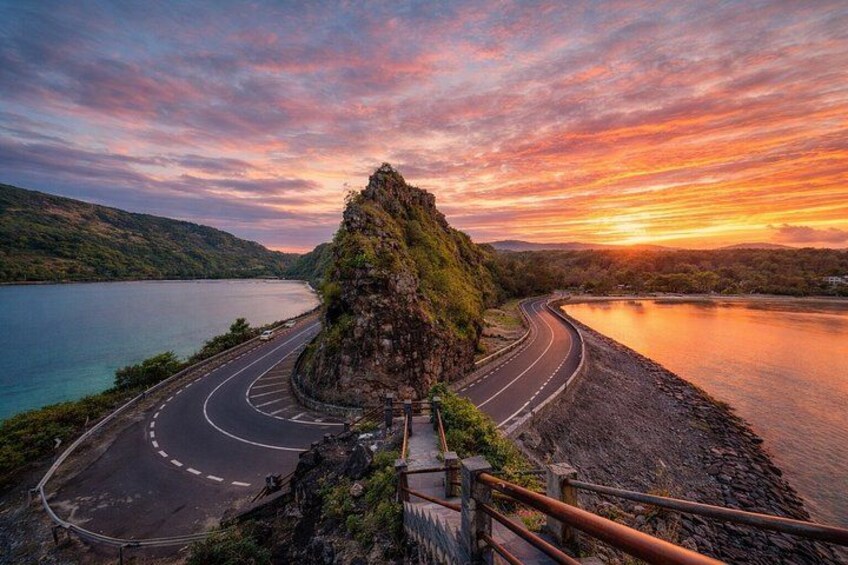 A winding road curving around a rocky outcrop with a sunset in the background. 2