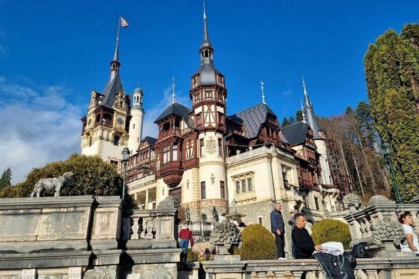 A historic castle with multiple towers and spires, a stone bridge in the foreground, and a clear blue sky. 1