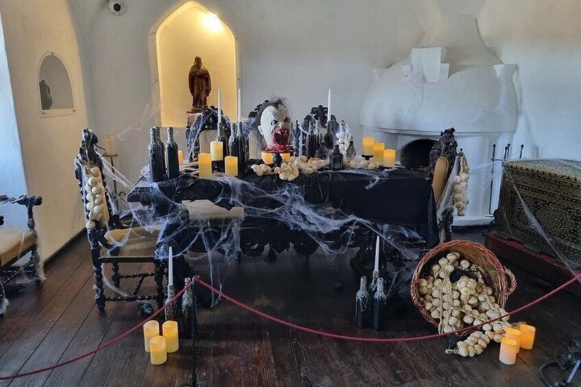 A room with a table covered in a black cloth, surrounded by candles, bottles, and a spider web decoration. 3
