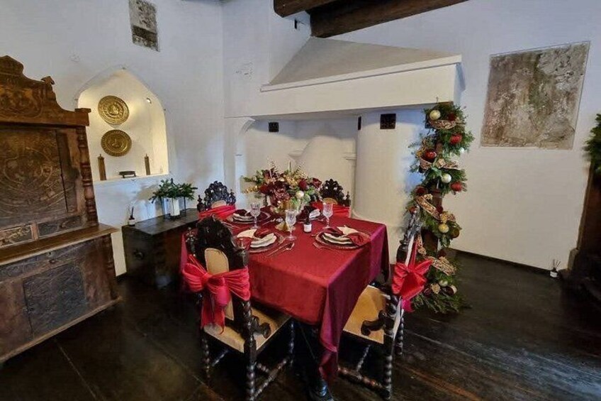 A dining room with a red tablecloth, wooden chairs, and Christmas decorations. 2