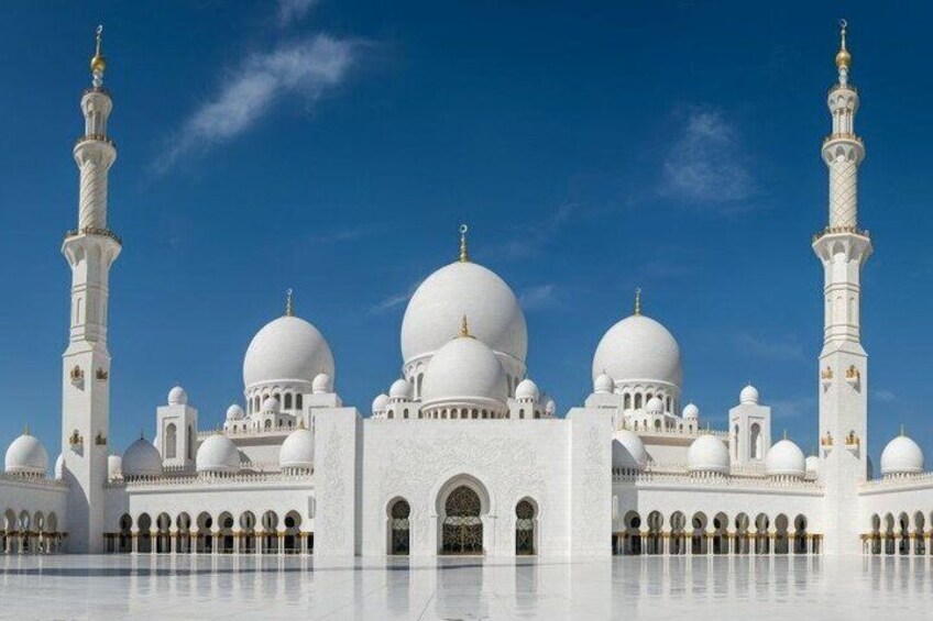 A white mosque with multiple domes and minarets under a clear blue sky. 1