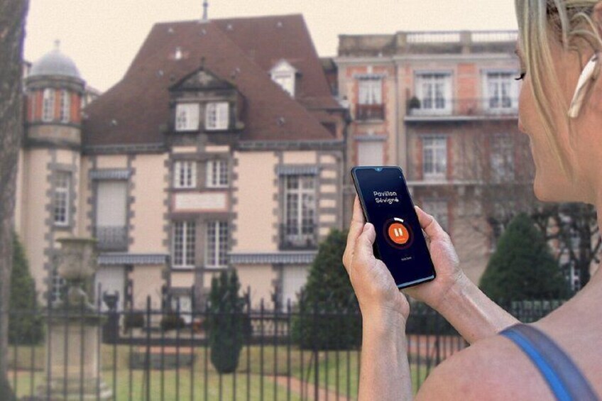 A person holding a smartphone with a map application, standing in front of a large, historic building with a prominent tower and multiple windows. 3
