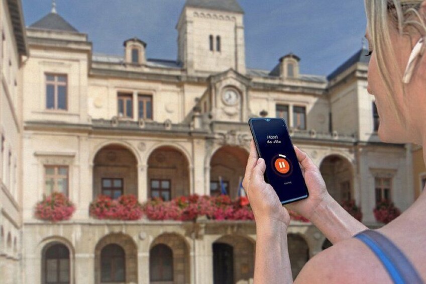 Una persona usando un teléfono inteligente con una interfaz de aplicación musical, de pie frente a un edificio histórico con arcos y una torre del reloj. 2