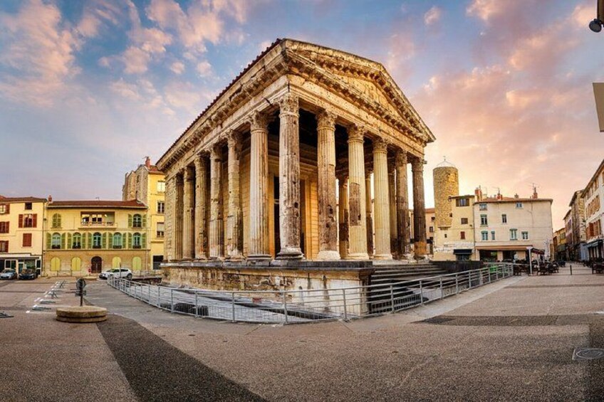 Un edificio clásico con columnas, una plaza adoquinada y edificios circundantes. 3