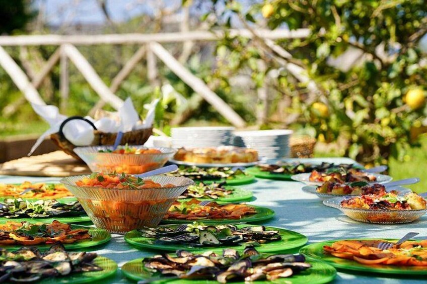 An outdoor buffet with various dishes on green plates, a wicker basket, and a wooden fence in the background. 3