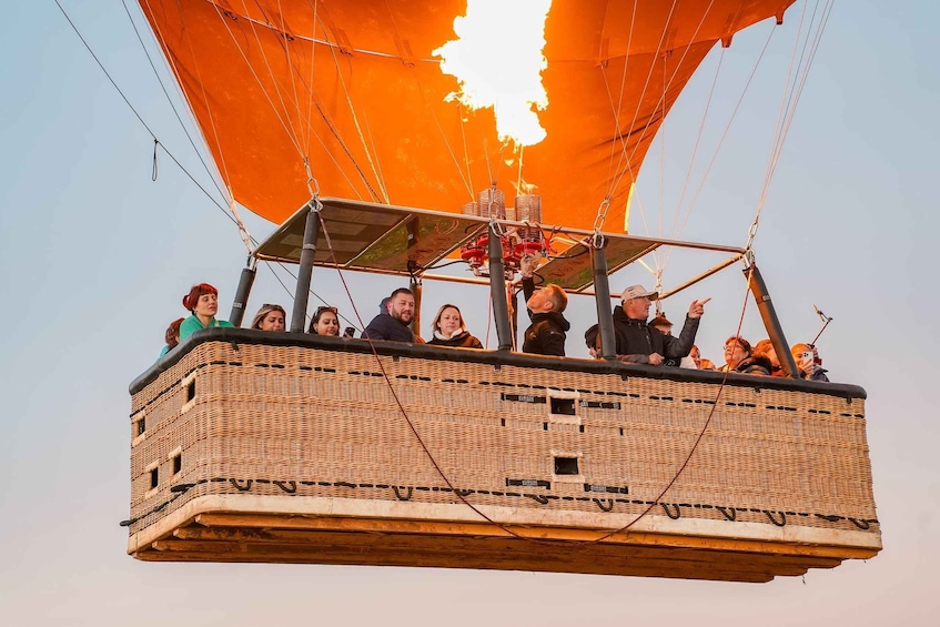 A wicker hot air balloon with passengers and a large orange canopy. 1