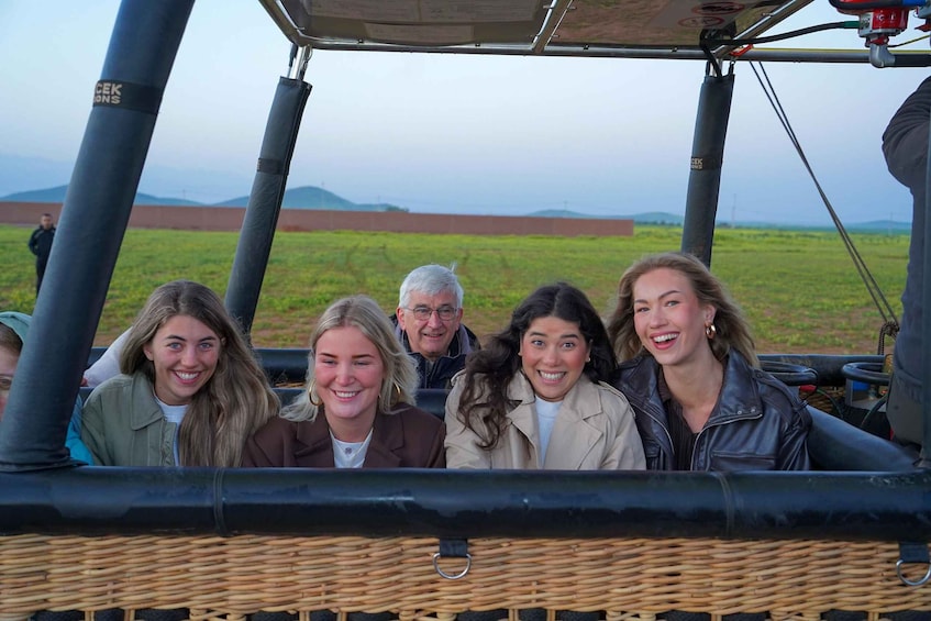 A group of people in a wicker-covered vehicle with a grassy field and mountains in the background. 4