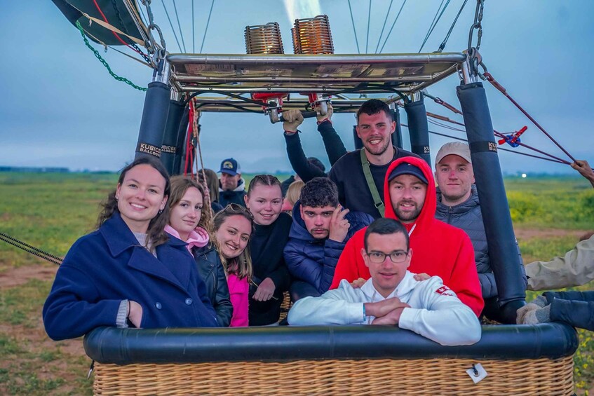 A group of people in a wicker basket attached to a hot air balloon with visible burners and cables. 5