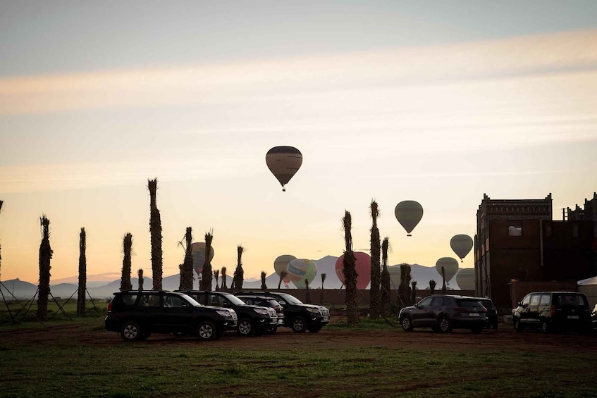 A field with parked cars and hot air balloons in the sky. 2
