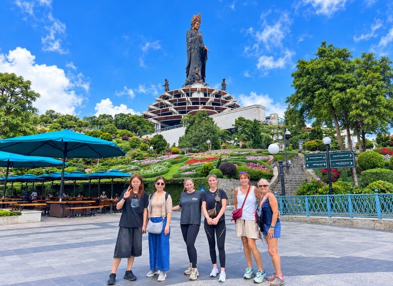 A group of people posing in front of a statue, with a building and landscaped garden in the background. 3