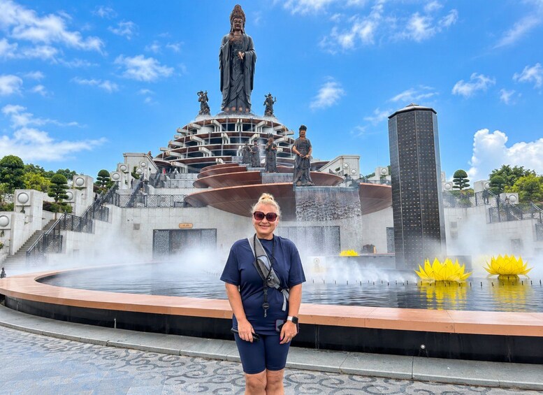 A person standing in front of a fountain with statues and a tall building in the background. 4