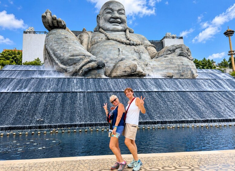 A large stone statue of a seated figure with outstretched arms, a water fountain in front, and a clear blue sky. 2