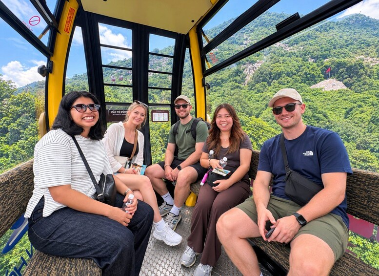 A group of people seated on a bench inside a cable car, overlooking a mountainous landscape. 1