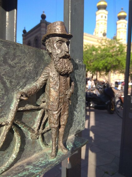 A bronze statue of a man with a bicycle, a building with domes, and a clear blue sky. 2