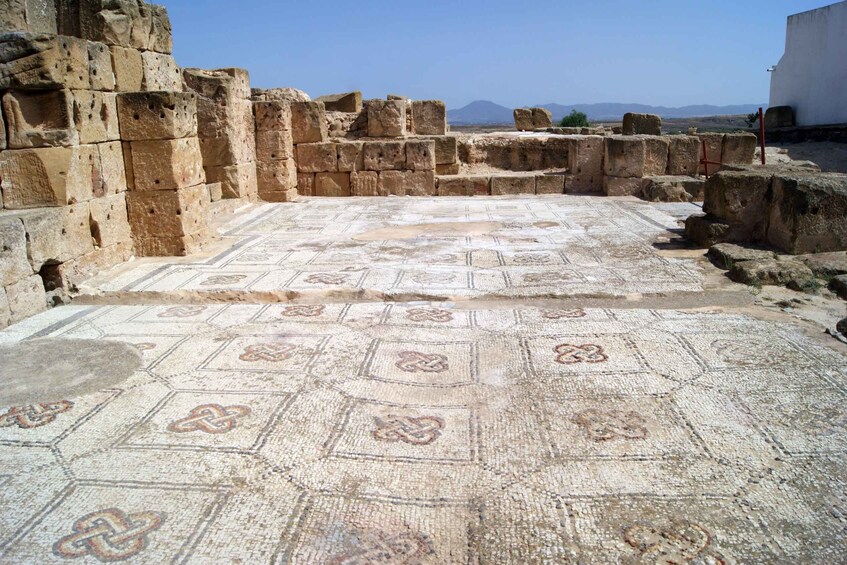 An ancient mosaic floor with geometric patterns, surrounded by stone walls and ruins. 4