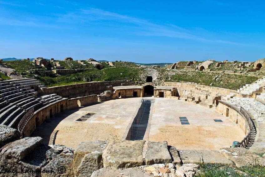 An ancient amphitheater with stone seating and a central stage. 5
