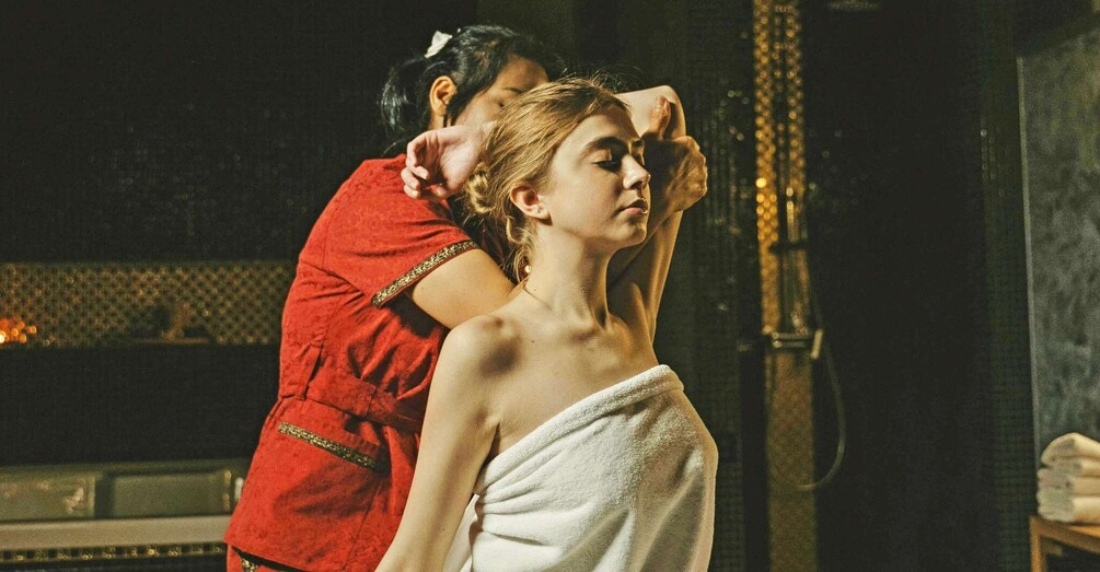 A person in a red robe attending to another person wrapped in a towel. 1