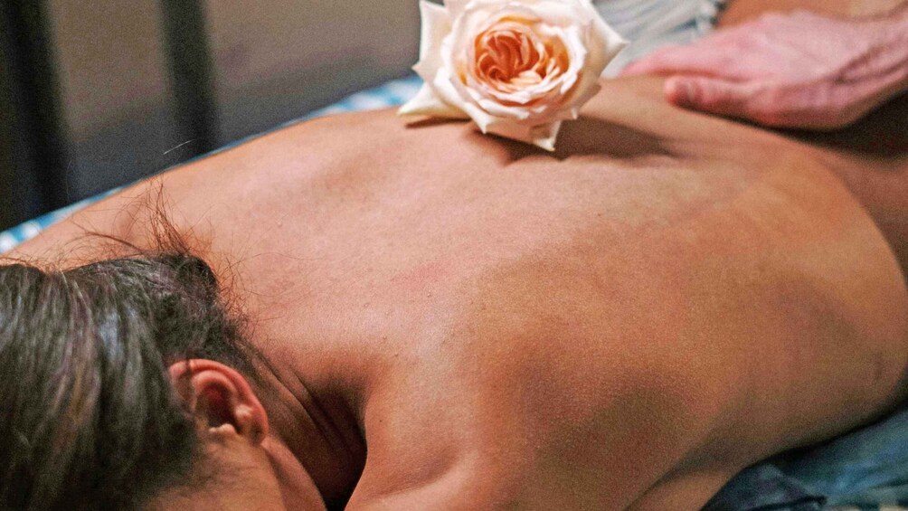 A person receiving a back massage with a rose placed on their back. 2