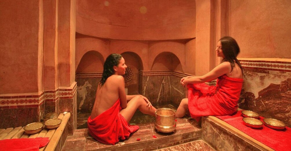 Two people in red robes sitting in a room with arches and a large golden pot. 5
