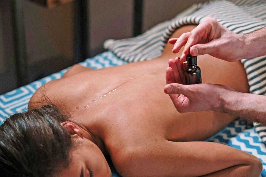 A person receiving a massage with a bottle of oil being applied to their back. 3