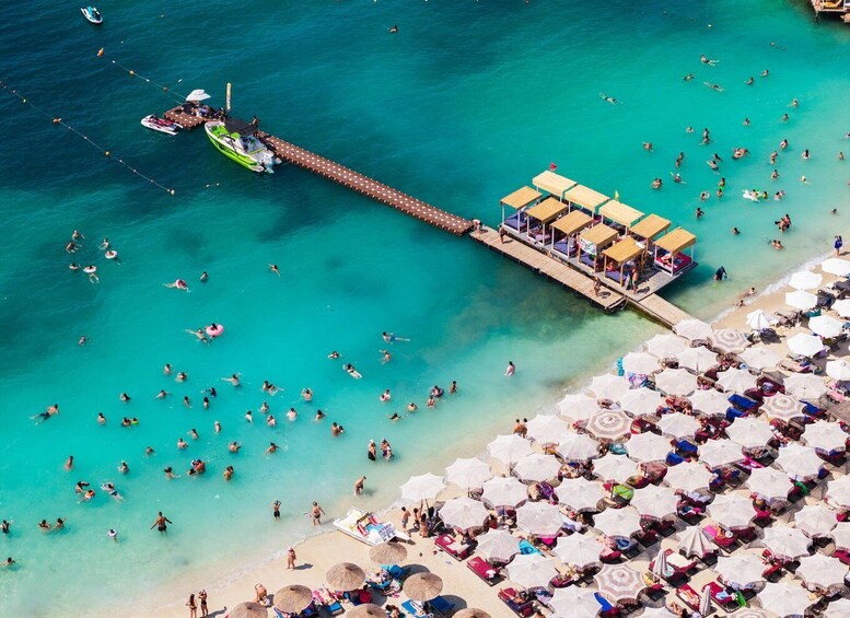 A beach with people swimming and sunbathing, a pier with a boat, and beach umbrellas. 4