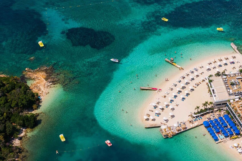 A tropical beach with clear turquoise waters, a sandy shore, and a resort area with umbrellas and lounge chairs. 2