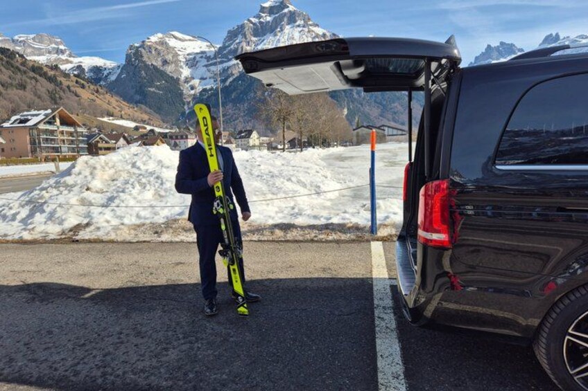 A person holding skis next to a vehicle with an open trunk in a snowy mountainous area. 3