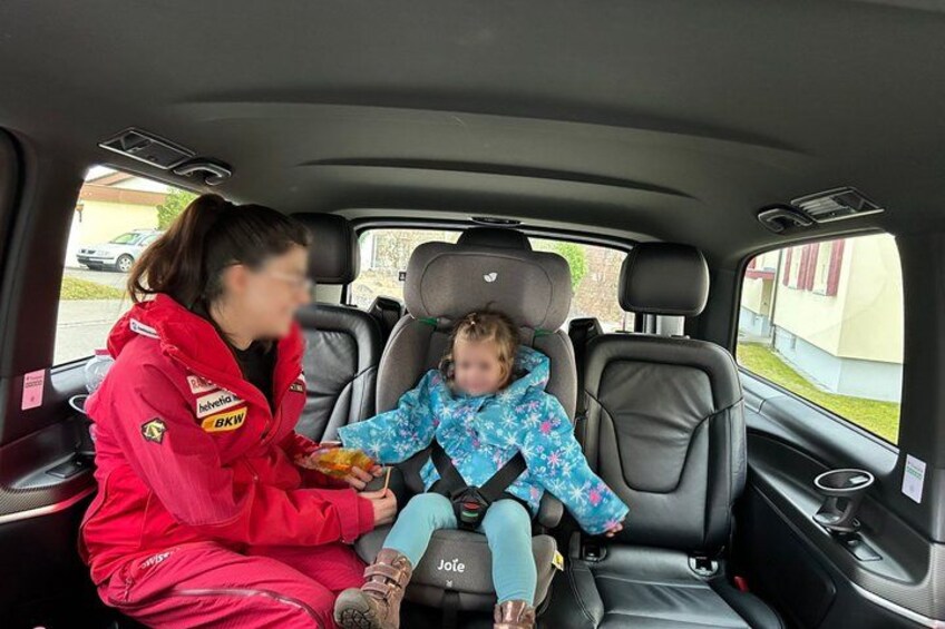 A woman in a red jacket and a child in a blue jacket seated in the back of a car. 4