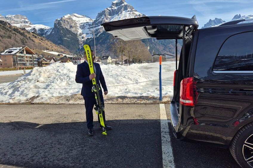 A person with skis standing next to a vehicle in a snowy area with mountains in the background. 4