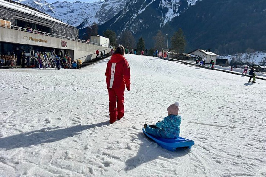 A snowy ski slope with skiers and a child sledding. 2
