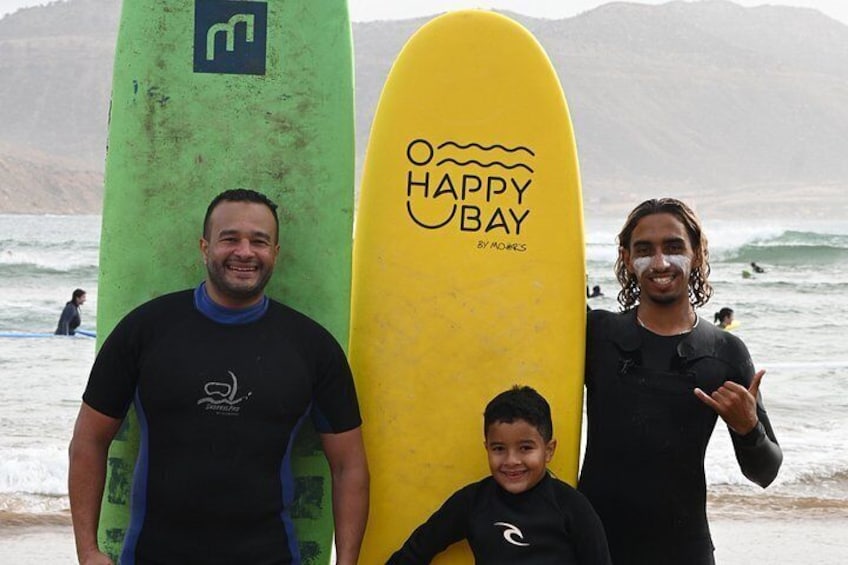 Three people standing on a beach with surfboards, ocean waves, and mountains in the background. 3