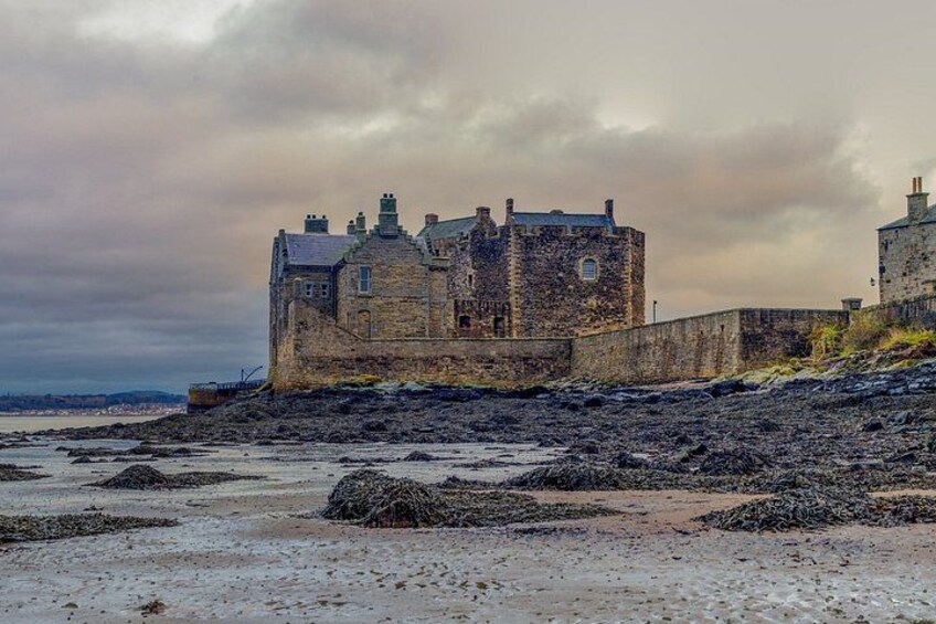 A historic stone castle by a rocky shoreline under a cloudy sky. 2