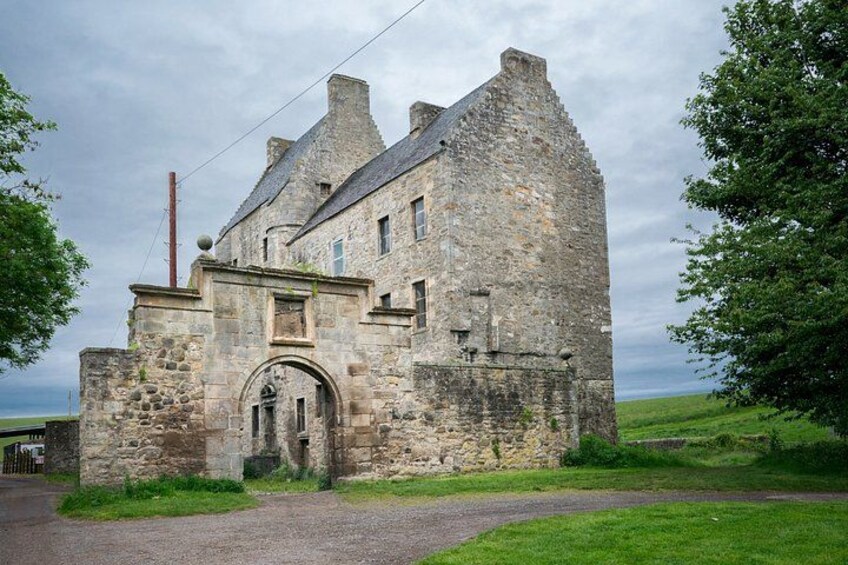 A stone castle with a large arched entrance, surrounded by grassy fields and a cloudy sky. 4